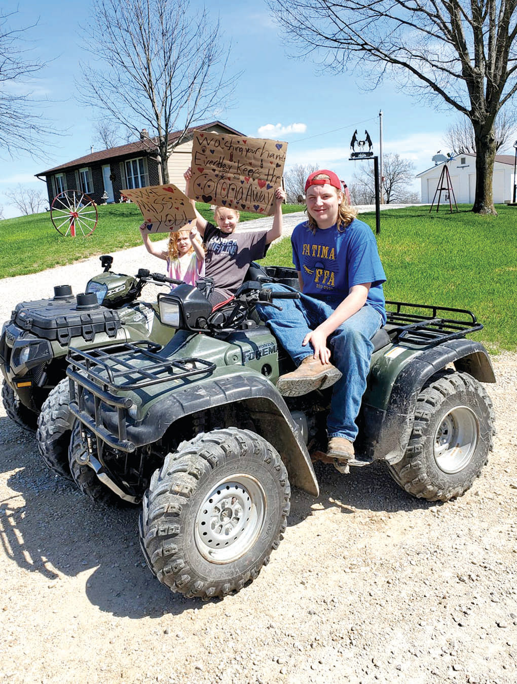 Ava, Riley and Jacob Buhr sit on their  ATV with signs during a recent Fatima teacher parade.
